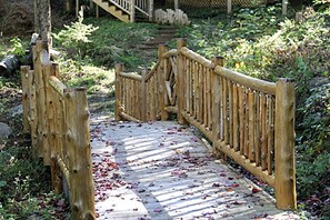 Eine Holzbrücke mit Geländern, umgeben von Grünpflanzen und einem Steinweg.