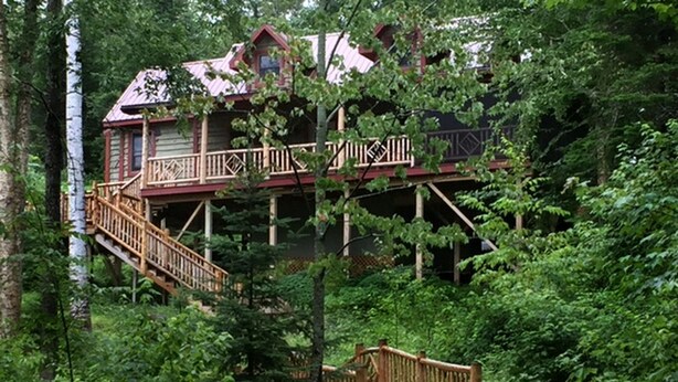 Una cabaña con terraza de madera y escalera, rodeada de un bosque denso.