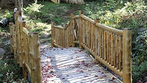 Un puente de madera con barandillas, rodeado de follaje y un sendero de piedra.
