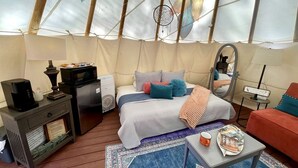 A cozy interior of a tent with a bed, a coffee table, a sofa, and a small table with a lamp.