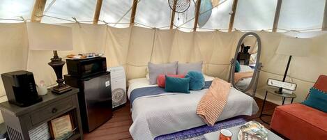 A cozy interior of a tent with a bed, a coffee table, a sofa, and a small table with a lamp.