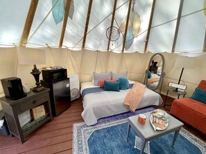 A cozy interior of a tent with a bed, a coffee table, a sofa, and a small table with a lamp.