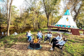 A group of people seated around a campfire in a forested area with a teepee structure in the background. - Serene Teepee Escape with Soulful Ambiance in Salt Lick, Kentucky (Salt Lick)