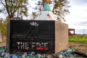 Uma estrutura de concreto com um logotipo e o texto 'THE EDGE' exposto, rodeada por fragmentos de vidro e uma tenda ao fundo.