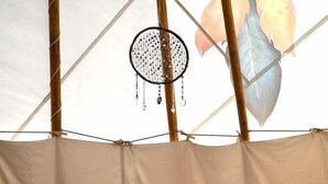 A bed with a patterned bedspread, multiple pillows, and a dreamcatcher hanging from the ceiling.