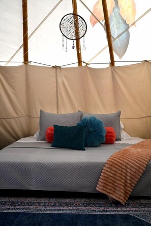 A bed with a patterned bedspread, multiple pillows, and a dreamcatcher hanging from the ceiling.