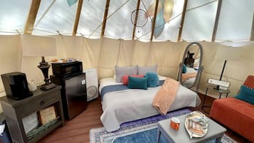 L’intérieur accueillant d’une tente, avec un lit, une table basse, un canapé et une petite table sur laquelle se trouve une lampe.