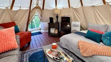 Interior aconchegante de uma tenda com uma cama, um sofá, uma mesinha e um abajur.