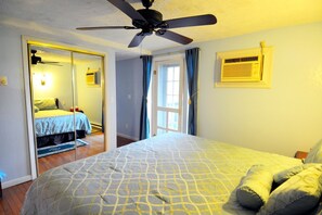 Un dormitorio con cama, ventilador de techo, ventana con cortinas y aire acondicionado instalado en la pared.