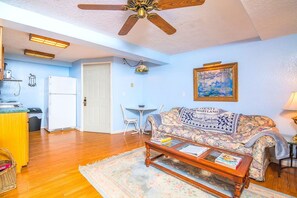 Una sala de estar con ventilador de techo, un sofá con una manta 'County Maryland', una mesa de centro y un comedor con mesa y sillas.