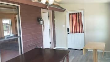 A room with a wooden table, a ceiling fan, a door with a curtain, and a small wooden stool.
