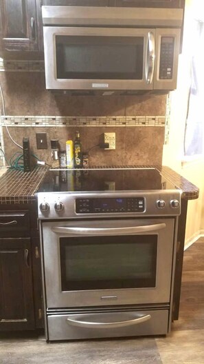 A kitchen with a built-in microwave and oven, a tiled backsplash, and a countertop with various items.