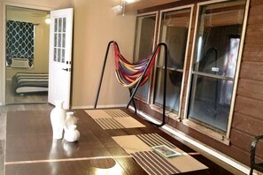 A room with a large window, a hammock, a door, and a small table with decorative items.