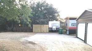Ein Kiesweg führt zu einer Garage, einem Holzzaun und einem Anhänger im Hintergrund.