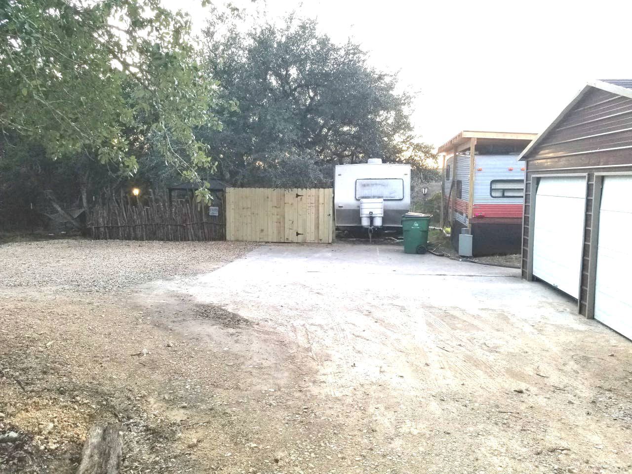 A gravel driveway leading to a garage, a wooden fence, and a trailer in the background.