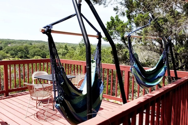 Une terrasse avec des garde-corps rouges, deux hamacs, une table et des chaises.
