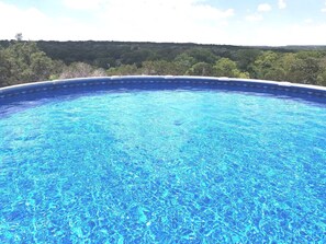 A clear blue swimming pool with a view of a forested landscape.