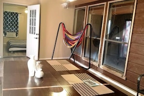 A room with a large window, a hammock, a door, and a small table with decorative items.