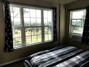 Un dormitorio con un ventanal grande, una cama con colcha a rayas y cortinas.