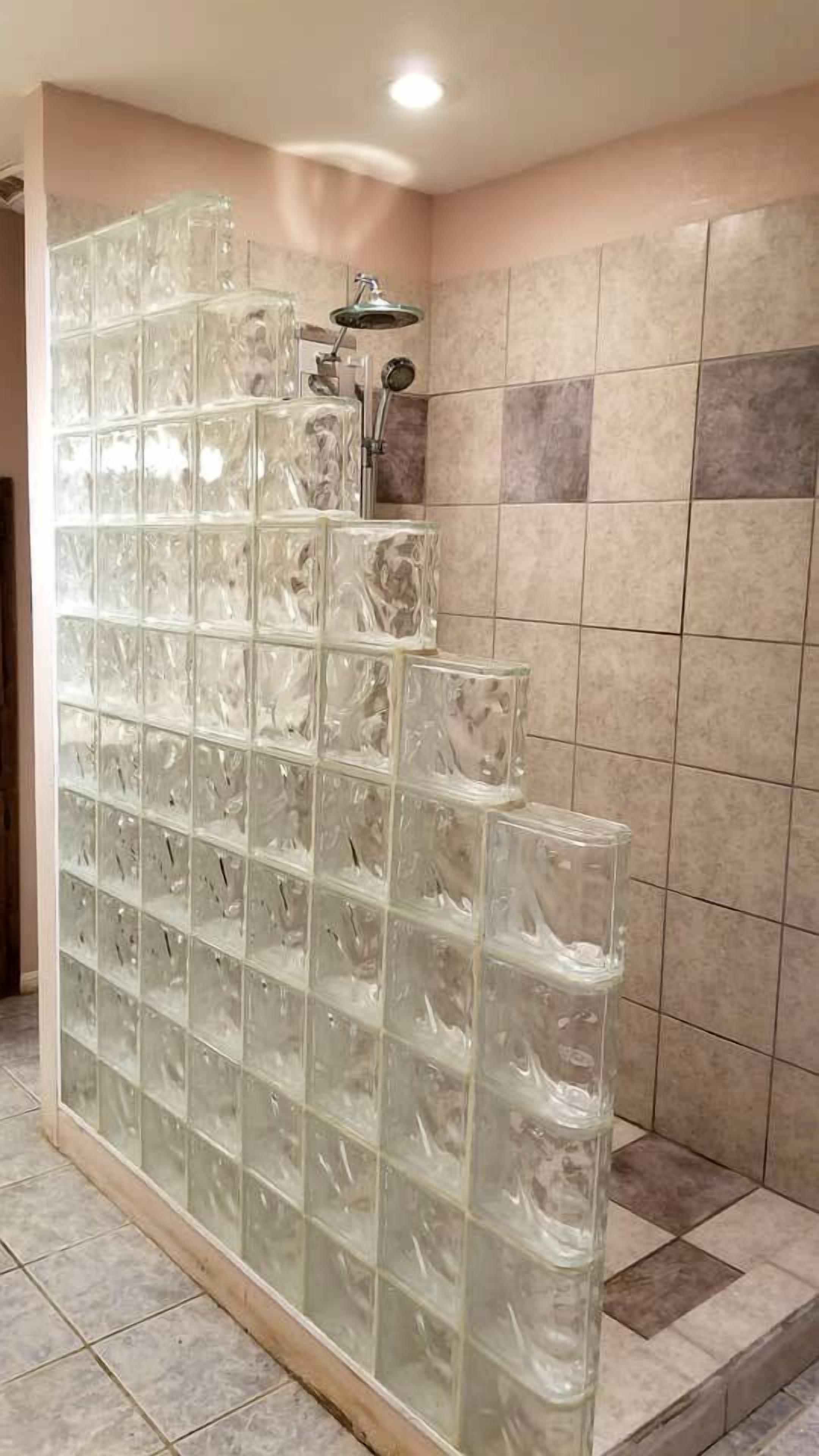 A bathroom with a glass block partition, a shower area, and tiled walls.