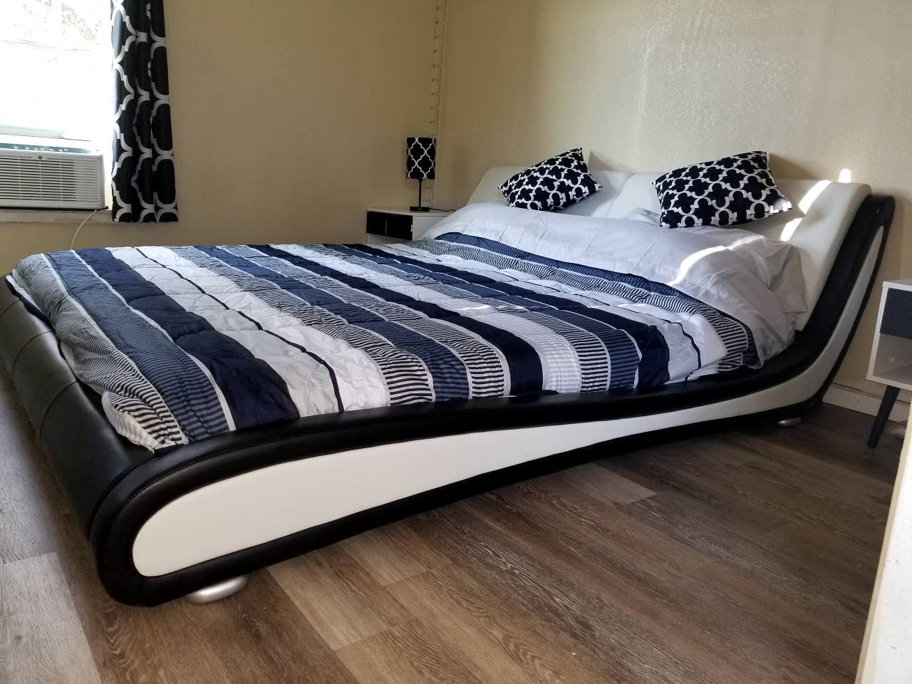 Una cama con colcha a rayas, una mesita de noche con lámpara y una ventana con cortinas.