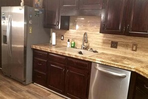 Una cocina con armarios de madera oscura, un refrigerador de acero inoxidable, un lavamanos con grifo y un lavavajillas.