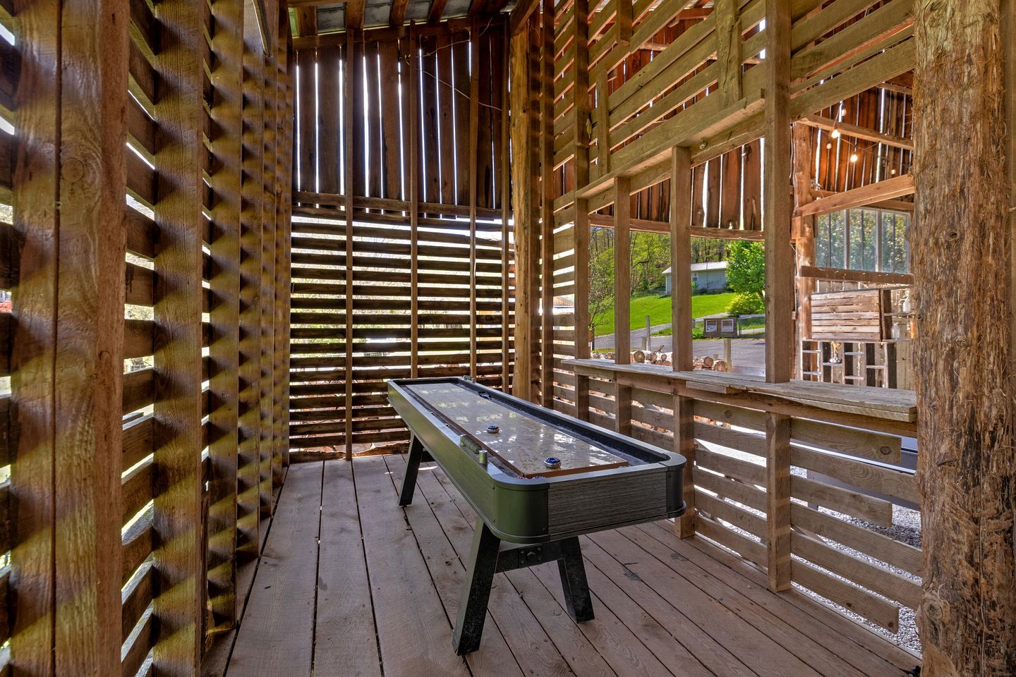 A pool table in a wooden-fenced outdoor area with a view of a green landscape.