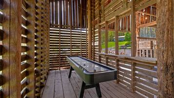 A pool table in a wooden-fenced outdoor area with a view of a green landscape.