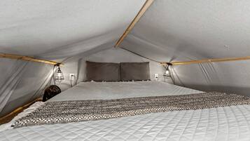 A tent-style room with a bed, two wall-mounted lights, and a fan.