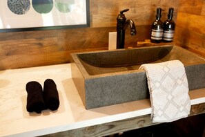 Un baño con un lavamanos de piedra, dos toallas, un grifo y dos botellas.