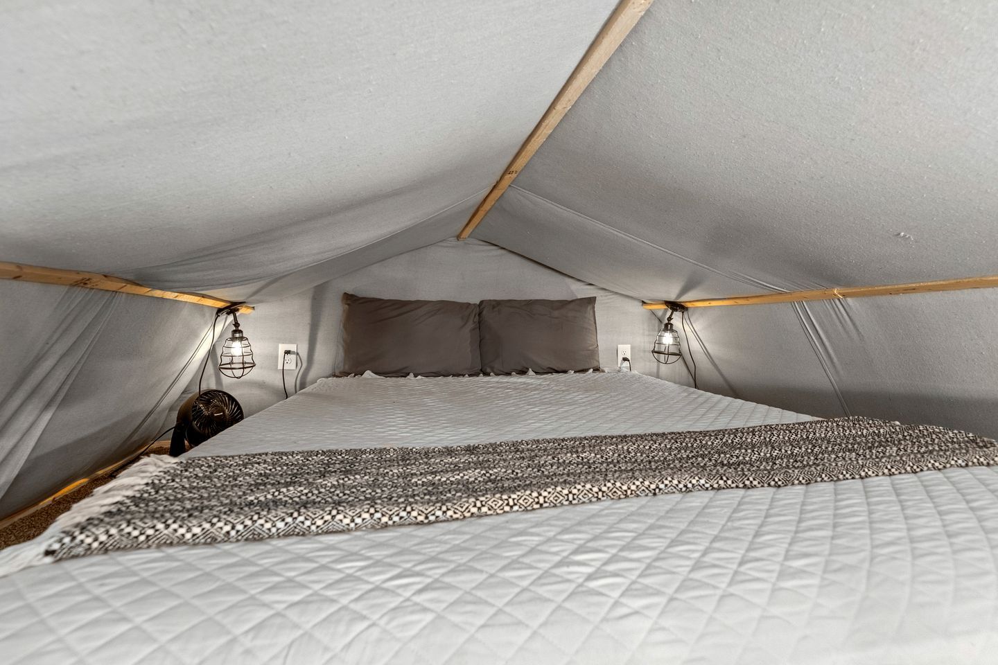 A tent-style room with a bed, two wall-mounted lights, and a fan.
