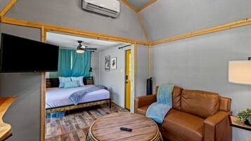 A compact room with a bed, a sofa, a small table, and a television.