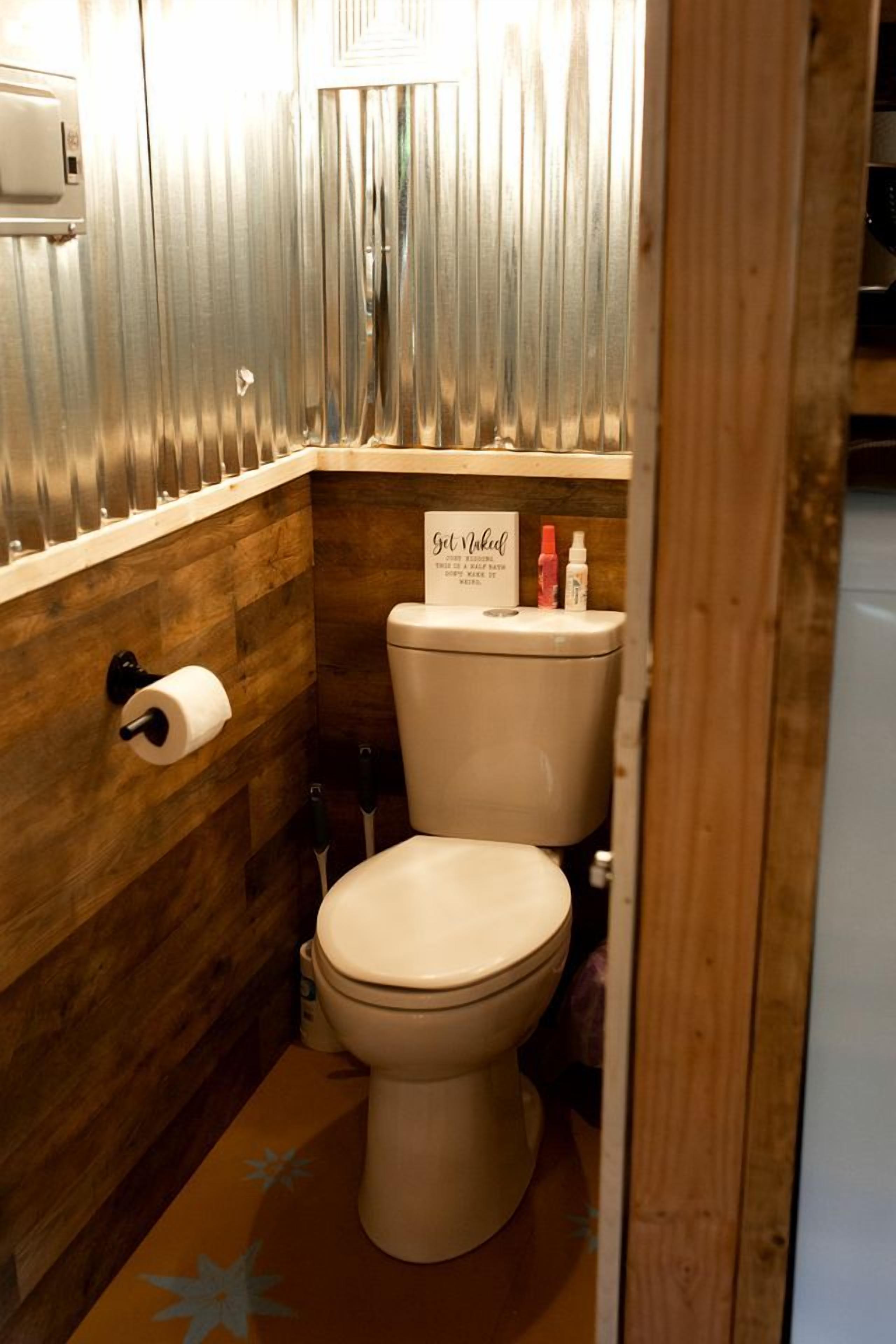 A compact bathroom with a wooden wall, a toilet, a hand dryer, and a sign on the wall.