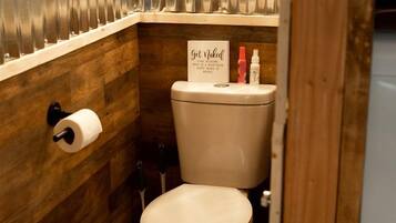 A compact bathroom with a wooden wall, a toilet, a hand dryer, and a sign on the wall.