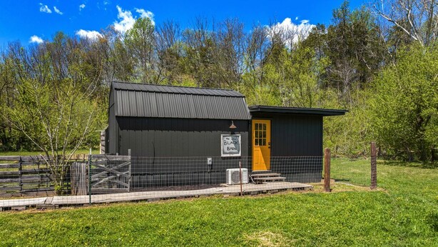A small, dark-colored barn with a yellow door and a fenced area. - Peaceful Cabin Retreat with Spa Features & Unique Farm Vibes in Newport, Tennessee (Newport)