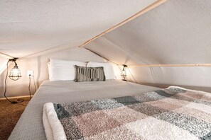 Une chambre à coucher avec un lit, des oreillers, une couverture et deux lampes fixées au mur.
