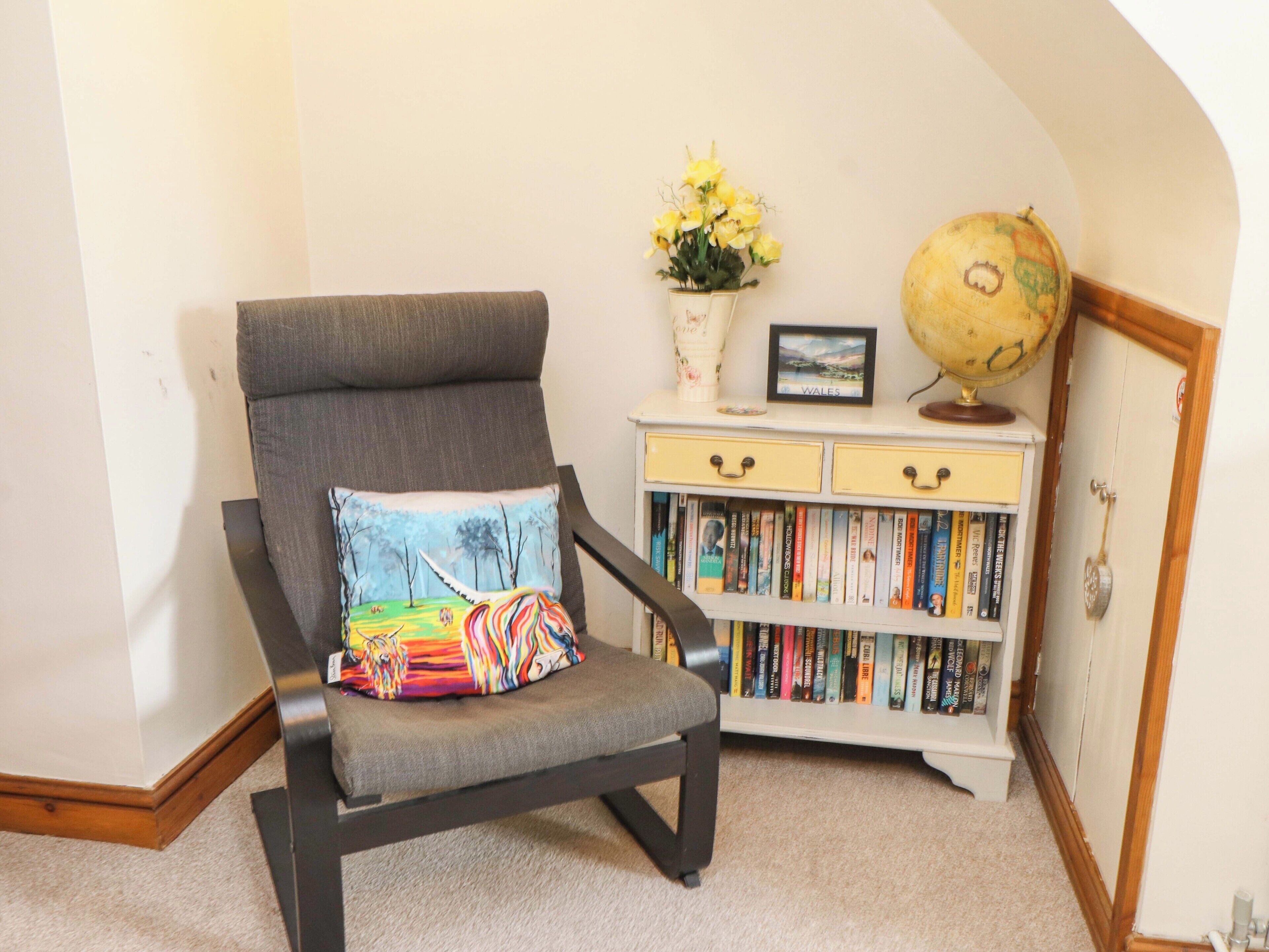 A chair with a colorful cushion, a bookshelf with books, a globe, and a vase with flowers.