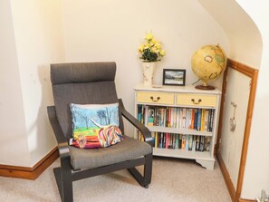 Una silla con un cojín colorido, una estantería con libros, un globo terráqueo y un florero con flores.