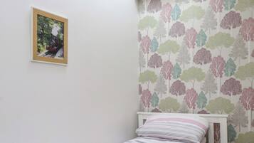 A bedroom with a bed, a nightstand, a lamp, and a wall with a tree pattern.