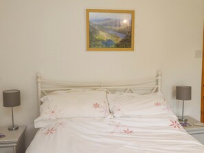 Ein Bett mit weißer Bettwäsche und floralem Muster, eine Nachttischlampe, ein Nachttisch und ein gerahmtes Landschaftsbild an der Wand.