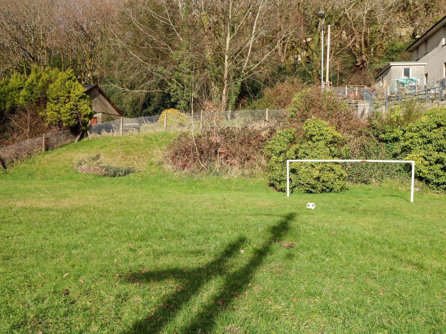 Un campo cubierto de hierba con un arco de fútbol, árboles y un edificio al fondo.
