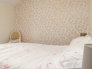 Un dormitorio con papel tapiz floral, cabecero de madera y cama con ropa de cama blanca.