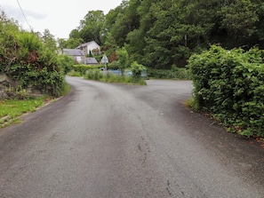 A rural road with a stone house, surrounded by dense greenery and trees.