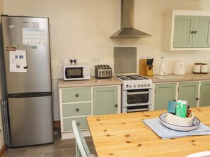 Uma cozinha equipada com geladeira, micro-ondas, torradeira, fogão, forno e armários verdes.