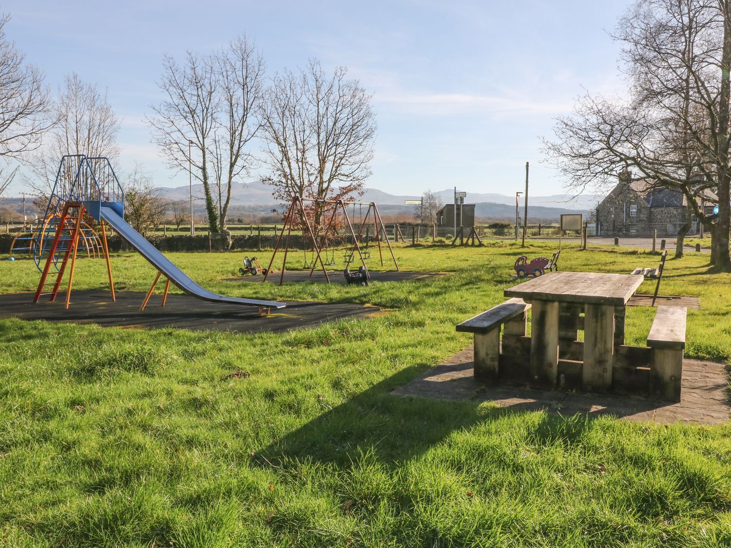 Un parque infantil con tobogán y columpios, una mesa de picnic y un edificio de piedra al fondo.