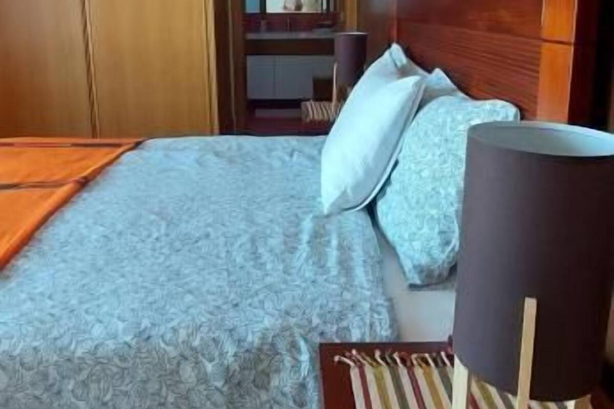 Ein Schlafzimmer mit einem Bett, einem Holzschrank, einem Spiegel und einem Nachttisch mit Lampe.