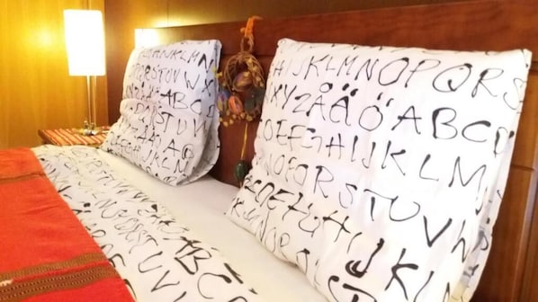 A bed with alphabet-patterned pillows, a red blanket, and a wooden headboard.