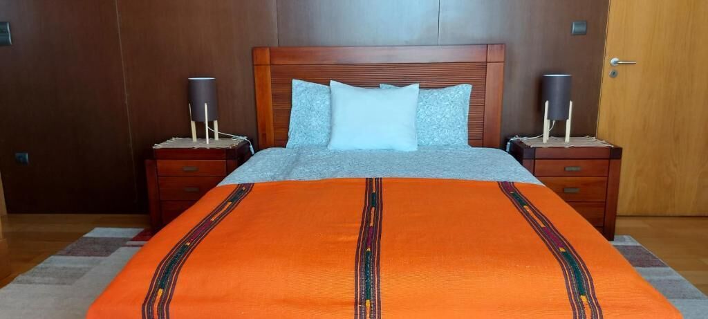 A bed with a patterned blanket, two bedside tables with lamps, and a wooden headboard.