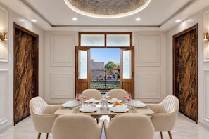 Uma sala de jantar com piso de mármore, uma mesa redonda posta para quatro pessoas e vista através de uma grande janela.