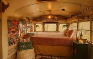 A cozy interior with a bed, a pillow with 'love' text, a small table with a candle, and a mural on the wall.